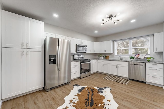 kitchen featuring stainless steel appliances, white cabinetry, sink, and light hardwood / wood-style floors