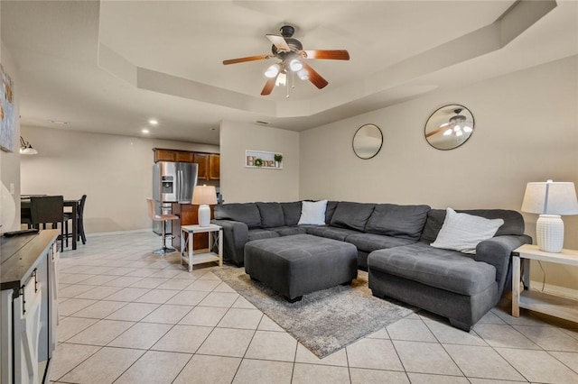 living room with light tile patterned floors, ceiling fan, and a tray ceiling