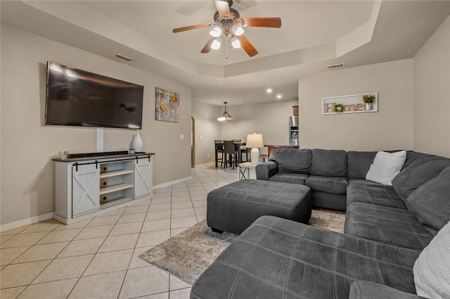 living room featuring light tile patterned floors, ceiling fan, and a tray ceiling