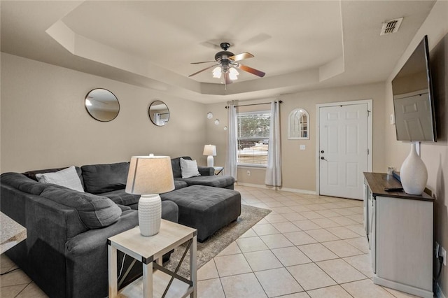 tiled living room with ceiling fan and a raised ceiling