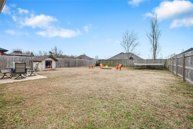 view of yard featuring a trampoline, a patio, a shed, and an outdoor fire pit