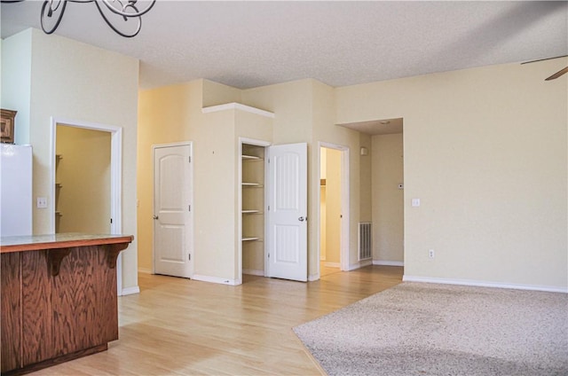 interior space with visible vents, light wood-style flooring, ceiling fan, a textured ceiling, and baseboards