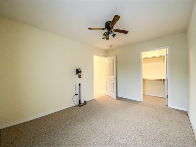 unfurnished bedroom with a spacious closet, a closet, carpet flooring, and a ceiling fan