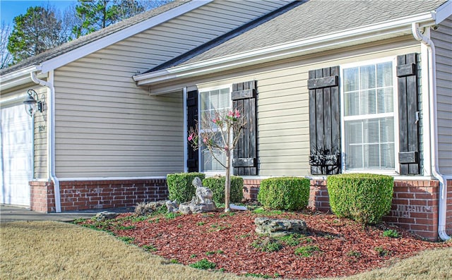 doorway to property featuring a garage, brick siding, and a shingled roof