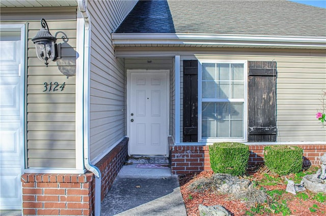 entrance to property with a garage, a shingled roof, and brick siding