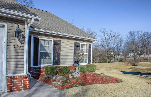 doorway to property with brick siding, roof with shingles, and a lawn