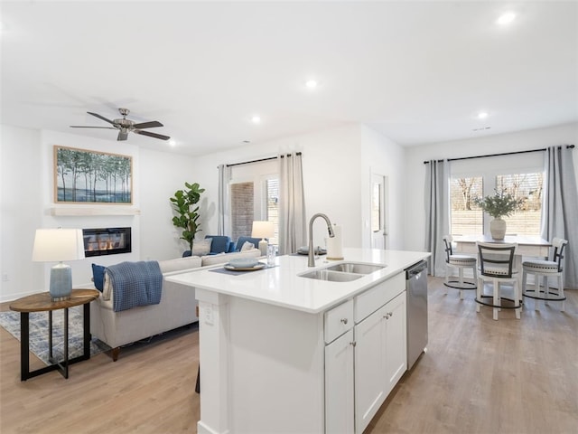 kitchen with sink, a kitchen island with sink, white cabinets, stainless steel dishwasher, and light wood-type flooring