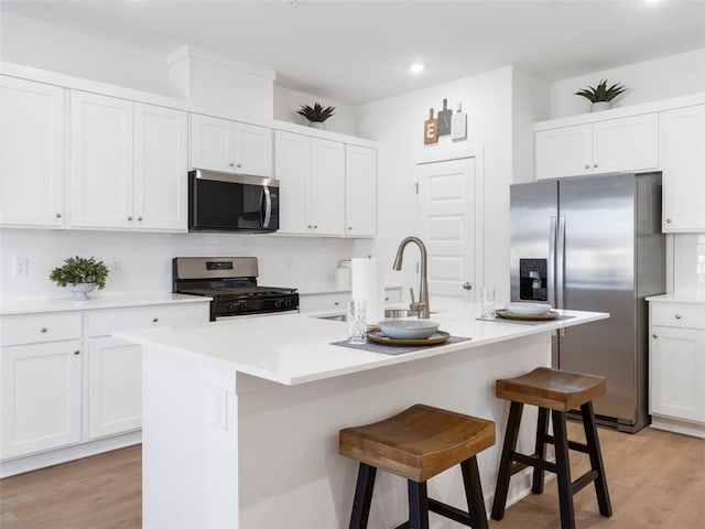 kitchen with appliances with stainless steel finishes, a kitchen island with sink, white cabinets, and a kitchen bar