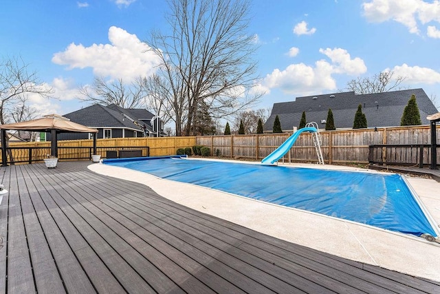 view of pool featuring a fenced backyard, a water slide, and a wooden deck