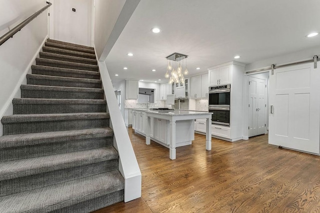 stairs with recessed lighting, wood finished floors, and a barn door