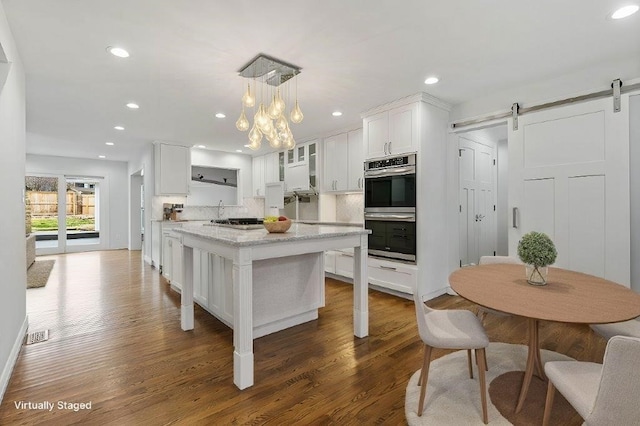kitchen featuring a barn door, stainless steel double oven, backsplash, and white cabinetry