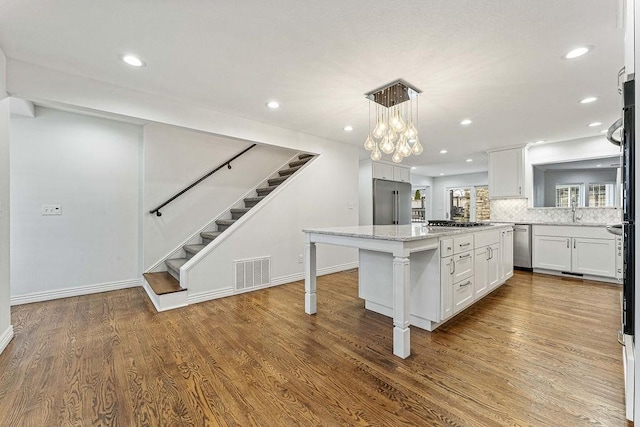 kitchen featuring wood finished floors, a center island, visible vents, and white cabinets