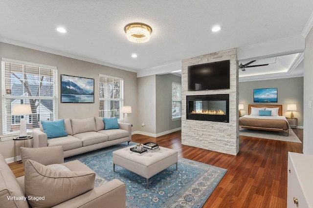living area with baseboards, ornamental molding, wood finished floors, a stone fireplace, and recessed lighting
