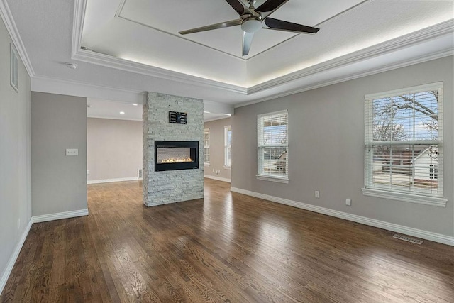 unfurnished living room with a raised ceiling, crown molding, a stone fireplace, and wood finished floors