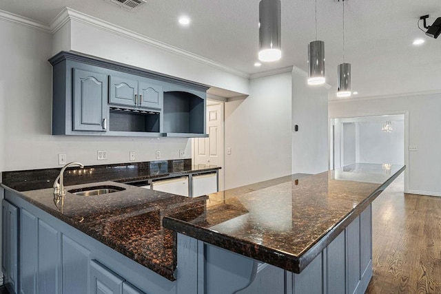 kitchen with dark wood-style floors, hanging light fixtures, ornamental molding, a sink, and dark stone countertops