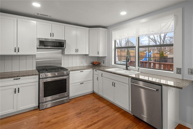 kitchen with sink, stone countertops, light wood-type flooring, stainless steel appliances, and white cabinets