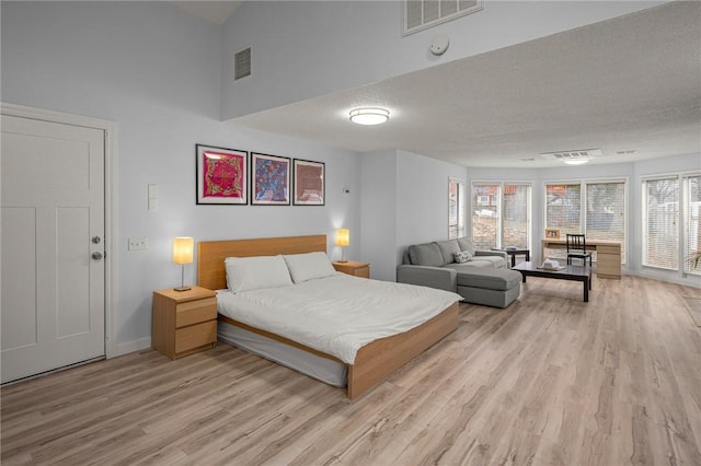 bedroom with a towering ceiling, light hardwood / wood-style floors, and a textured ceiling