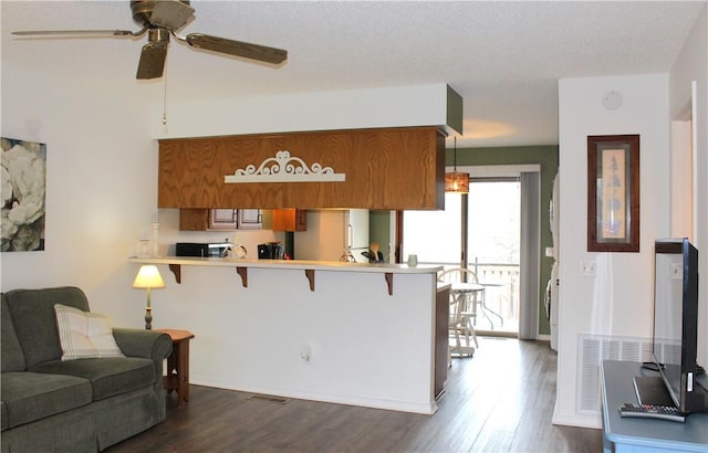 kitchen with pendant lighting, a breakfast bar area, ceiling fan, dark hardwood / wood-style floors, and kitchen peninsula