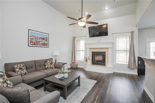 living room with ceiling fan, dark wood-type flooring, a tile fireplace, and a healthy amount of sunlight