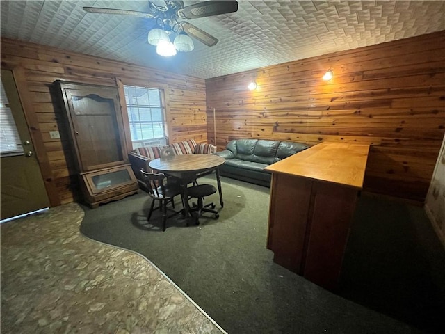 carpeted dining area with ceiling fan and wooden walls