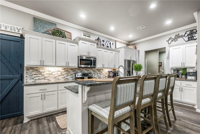 kitchen with a center island with sink, a kitchen breakfast bar, white cabinets, and appliances with stainless steel finishes