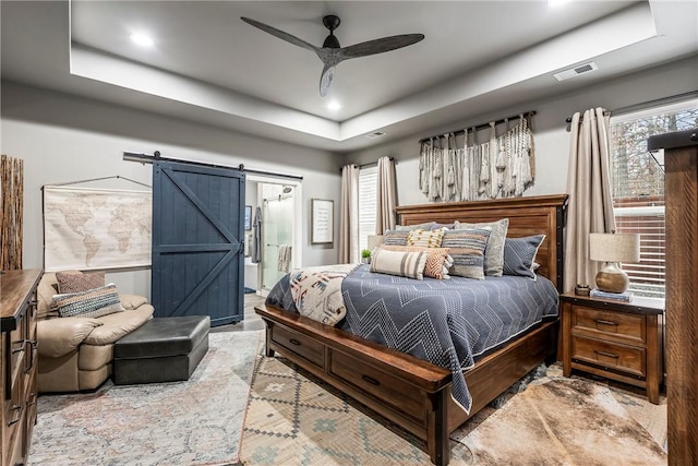 bedroom with connected bathroom, a barn door, a raised ceiling, and ceiling fan