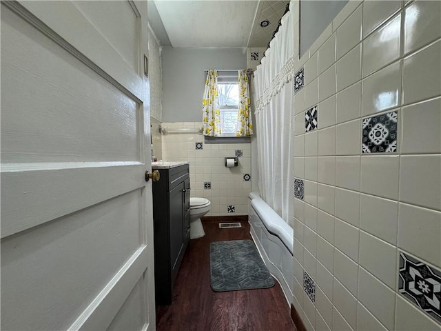 full bathroom with shower / tub combo with curtain, tile walls, hardwood / wood-style floors, vanity, and toilet