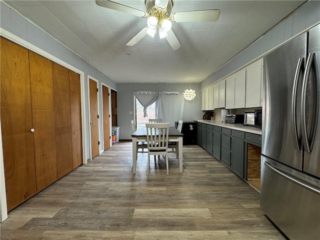 kitchen with ceiling fan with notable chandelier, pendant lighting, stainless steel fridge, and light wood-type flooring