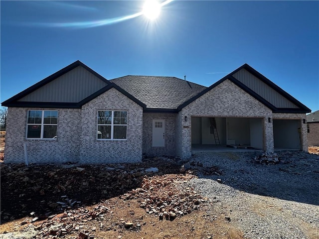 view of front facade featuring a garage, gravel driveway, brick siding, and a shingled roof