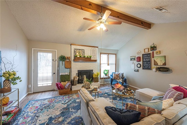 living room featuring vaulted ceiling with beams, a wealth of natural light, a fireplace, and light hardwood / wood-style flooring