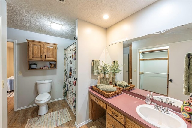 bathroom with curtained shower, hardwood / wood-style floors, vanity, toilet, and a textured ceiling