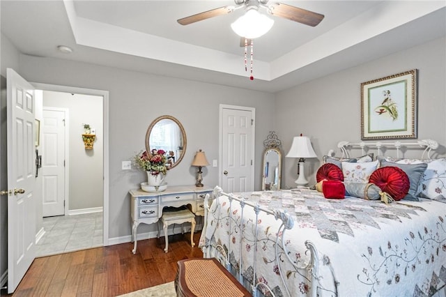 bedroom with a raised ceiling, hardwood / wood-style flooring, and ceiling fan