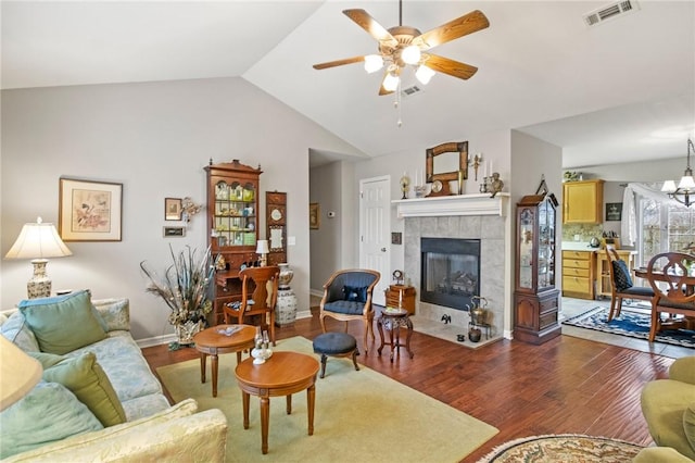 living room with dark wood-type flooring, ceiling fan with notable chandelier, vaulted ceiling, and a tile fireplace