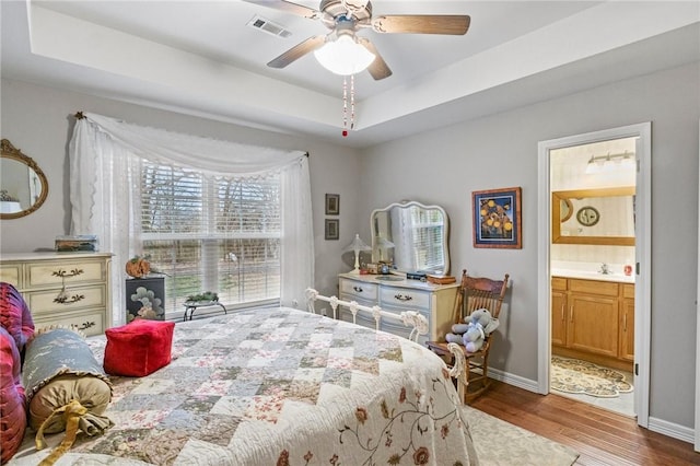 bedroom with ceiling fan, ensuite bath, a raised ceiling, and hardwood / wood-style floors