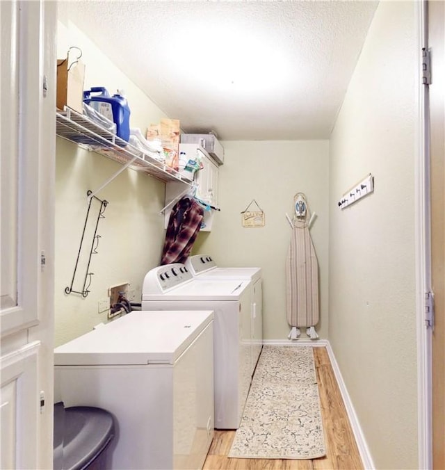 clothes washing area featuring cabinets, separate washer and dryer, and light wood-type flooring