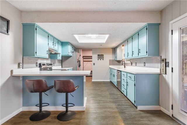 kitchen with blue cabinets, sink, a skylight, kitchen peninsula, and stainless steel appliances