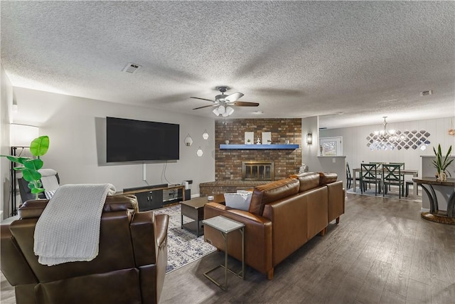 living room featuring a brick fireplace, a textured ceiling, dark hardwood / wood-style floors, and ceiling fan