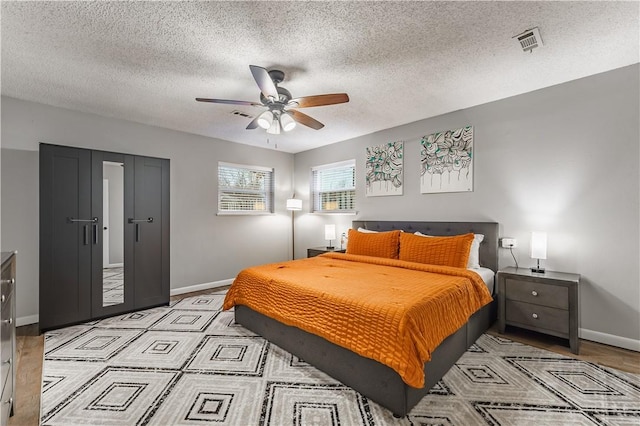 bedroom with a ceiling fan, baseboards, visible vents, light wood-style floors, and a textured ceiling