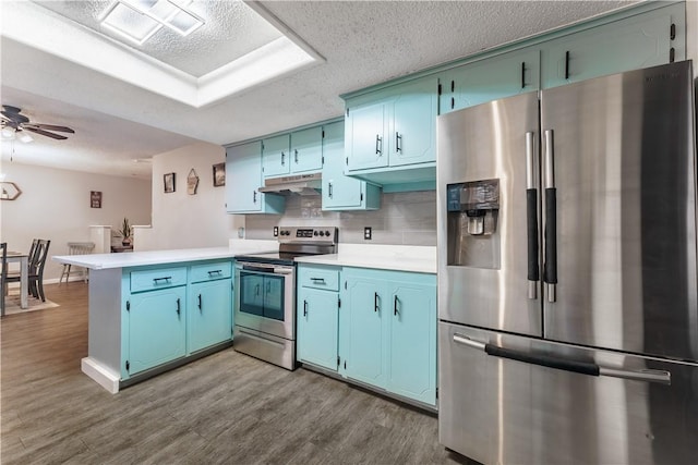 kitchen with blue cabinets, under cabinet range hood, a textured ceiling, stainless steel appliances, and a peninsula