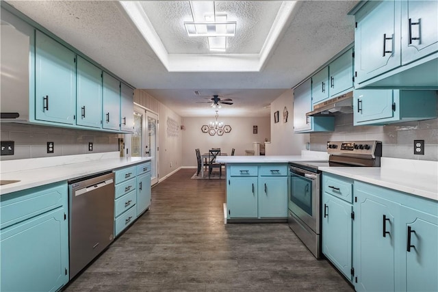 kitchen featuring under cabinet range hood, dark wood finished floors, appliances with stainless steel finishes, a peninsula, and a raised ceiling