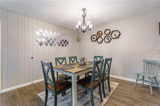 dining space with a chandelier, a textured ceiling, baseboards, and wood finished floors