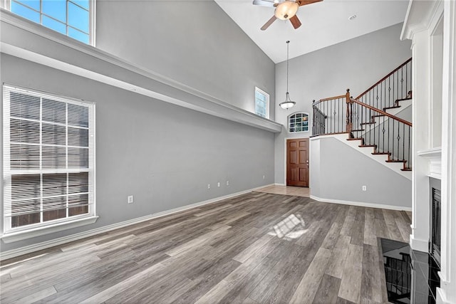 unfurnished living room featuring wood-type flooring, ceiling fan, and a high ceiling