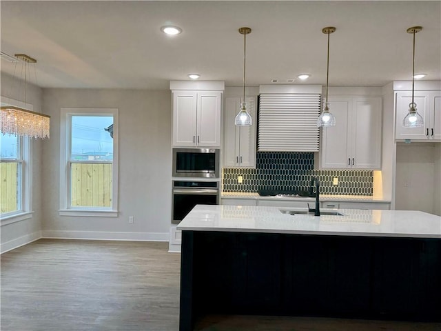 kitchen with pendant lighting, sink, appliances with stainless steel finishes, an island with sink, and white cabinets