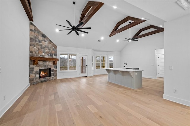 unfurnished living room with beamed ceiling, ceiling fan, a stone fireplace, and light hardwood / wood-style floors