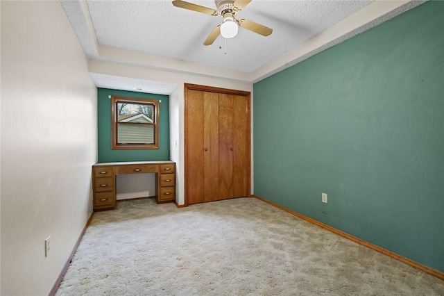 unfurnished bedroom with ceiling fan, light colored carpet, a closet, and a textured ceiling