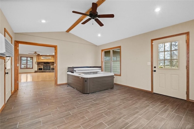 interior space with ceiling fan, a stone fireplace, and lofted ceiling with beams