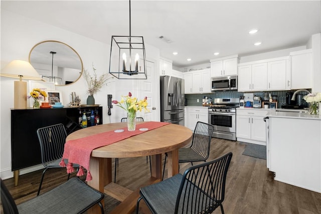 kitchen with pendant lighting, appliances with stainless steel finishes, white cabinetry, dark hardwood / wood-style flooring, and decorative backsplash