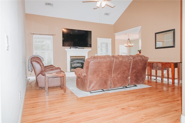 living room with ceiling fan with notable chandelier, high vaulted ceiling, and light hardwood / wood-style flooring