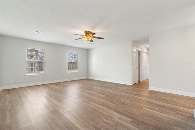 empty room with a ceiling fan, light wood-type flooring, visible vents, and baseboards