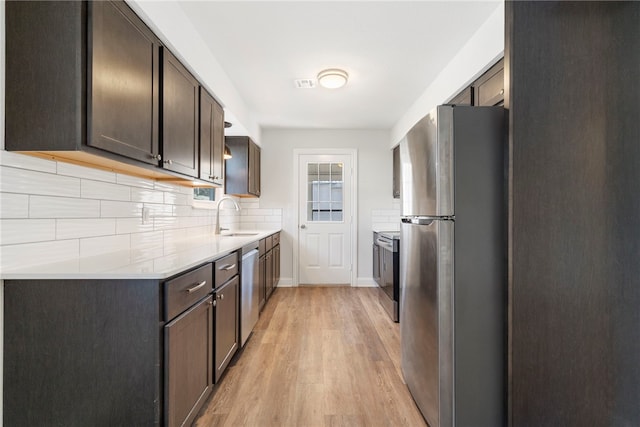 kitchen featuring stainless steel appliances, light countertops, light wood-style flooring, decorative backsplash, and dark brown cabinetry